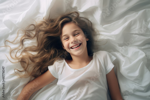 Pretty happy smiling kid in bed in the morning on clean white linens. A healthy sleep routine. 
