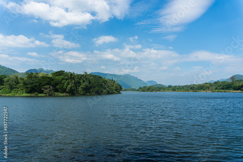 Beautiful lakeside view from a small lake in Kanchanaburi Thailand, with green trees, blue sky and sunlight