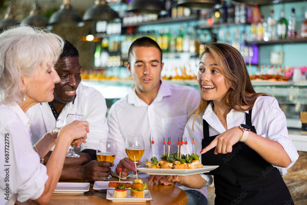Portrait of positive waiter with serving tray meeting restaurant guests