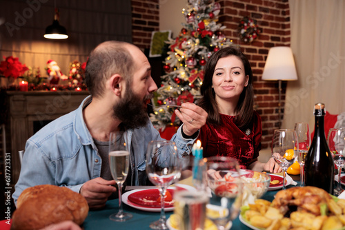 Couple attending christmas dinner with family, woman celebrating xmas winter holiday with friends at festive event. People feeling happy eating food and drinking wine at home.