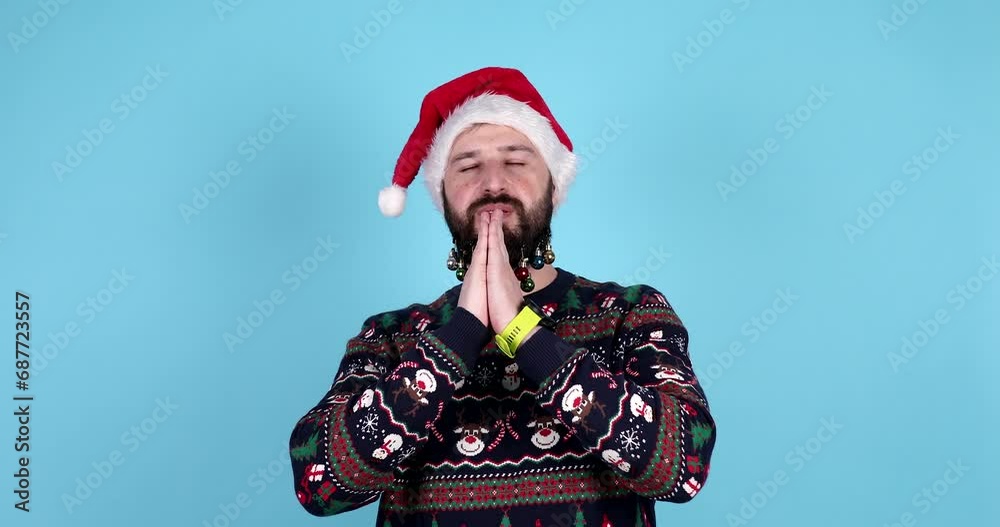 Young bearded man with santa claus hat praying on blue background. Young bearded man with santa claus hat praying on blue background.