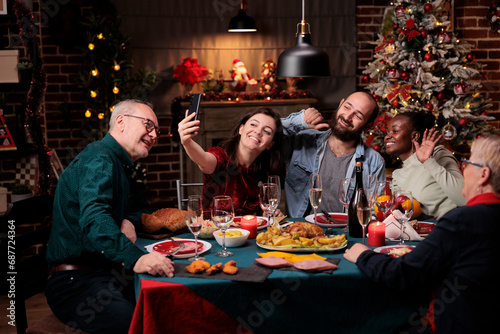 Family taking photos at christmas dinner with delicious food and glasses of wine  making memories during december holiday event. Diverse people having fun with pictures on smartphone at home.