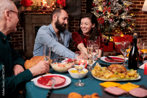 Cute people meeting family at home on christmas eve holiday, gathering around table with persons to eat meal and drink alcohol. Young persons talking to relatives during december festivity.