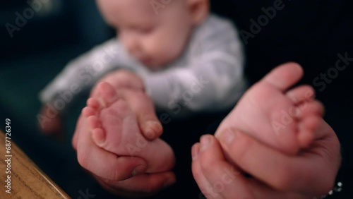 Dad's hands hold the tiny feet of his baby. Father tickles and claps son's feet. Close up. Blurred backdrop. photo