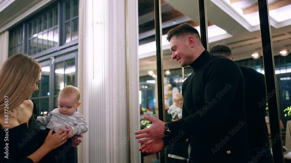 Caucasian woman with child in hands stands in front of the mirrors. Father stretches hands to his son and takes him lifting up. Low angle view. Caucasian woman with child in hands stands in front of the mirrors. Father stretches hands to his son and takes him lifting up. Low angle view.