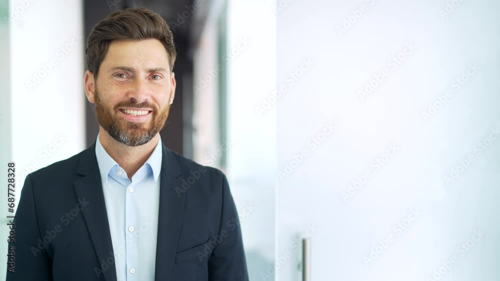 Portrait of a successful businessman in a formal suit standing in a business office. Confident smiling bearded entrepreneur looking at camera. Template for advertising. Copy empty space. Close up Portrait of a successful businessman in a formal suit standing in a business office. Confident smiling bearded entrepreneur looking at camera. Template for advertising. Copy empty space. Close up