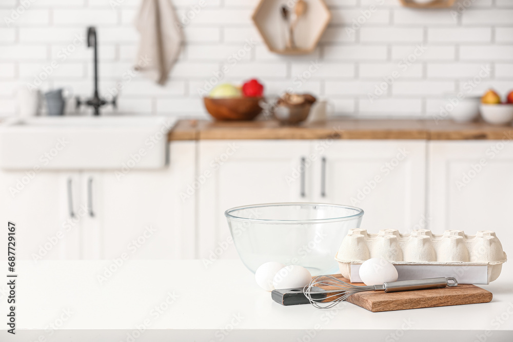 Package with eggs, whisk and glass bowl on table in kitchen