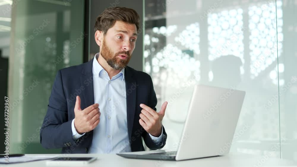 Angry dissatisfied businessman in a formal suit arguing on a video call using a laptop sitting at workplace in business office. Excited male boss emotionally talks with a subordinate about problems Angry dissatisfied businessman in a formal suit arguing on a video call using a laptop sitting at workplace in business office. Excited male boss emotionally talks with a subordinate about problems
