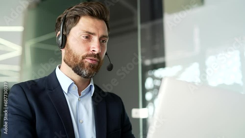 A corporate operator who works in customer support speaks on a video call using a laptop. Call center agent in wireless headset helping clients with complaints in office. Online consultation. Close up photo