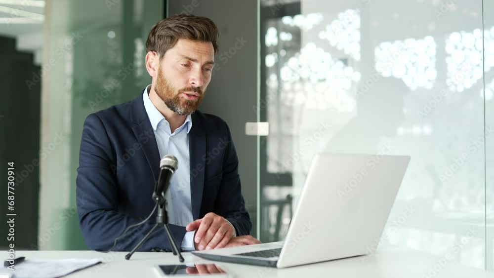 Confident tutor in formal suit talking on video call using laptop and microphone sitting at workplace in office. Coach conducts an online business training, seminar, class, course or webinar remotely Confident tutor in formal suit talking on video call using laptop and microphone sitting at workplace in office. Coach conducts an online business training, seminar, class, course or webinar remotely