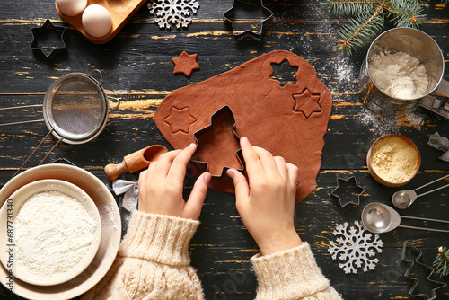 Woman preparing tasty Christmas gingerbread cookies on black wooden background