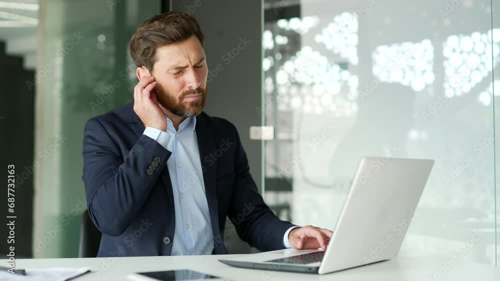 Earache. Sick businessman suffers from ear pain while working on laptop sitting in office. Upset male touches his ear with his fingers. He has furuncle, shingles, eczema, ear diseases, otitis media Earache. Sick businessman suffers from ear pain while working on laptop sitting in office. Upset male touches his ear with his fingers. He has furuncle, shingles, eczema, ear diseases, otitis media