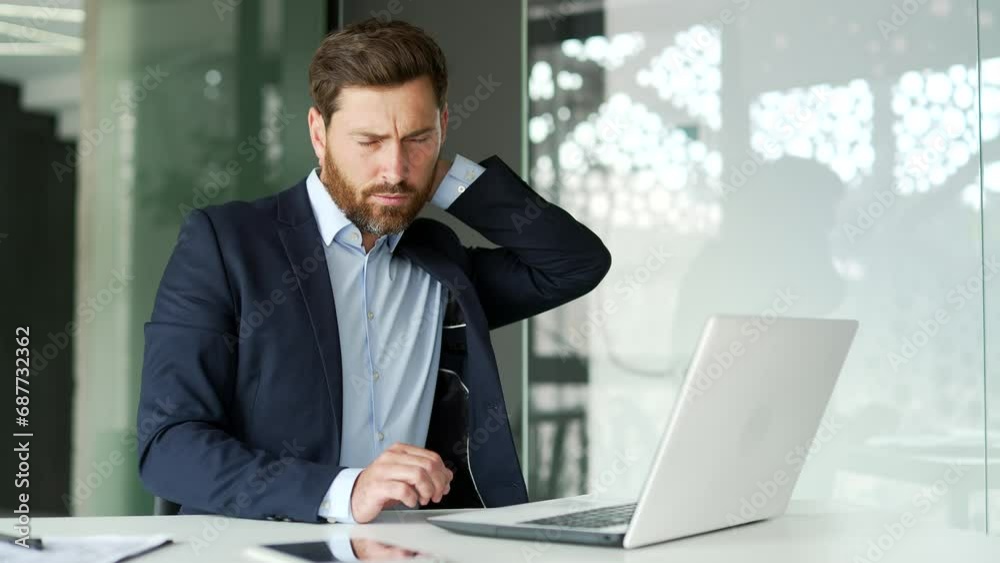 Tired businessman suffering from neck pain while working on laptop while sitting at desk at workplace in business office. Upset entrepreneur in formal suit massages and rubs sore muscles, stretches Tired businessman suffering from neck pain while working on laptop while sitting at desk at workplace in business office. Upset entrepreneur in formal suit massages and rubs sore muscles, stretches