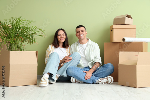 Happy young couple with moving boxes sitting near green wall © Pixel-Shot