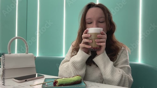 in girl's hands mug with cappuccino latte with pistachios and pieces of dried fruit raspberries a glass with foam of a delicious hot drink white blouse her hair down on a light green turquoise. Azure