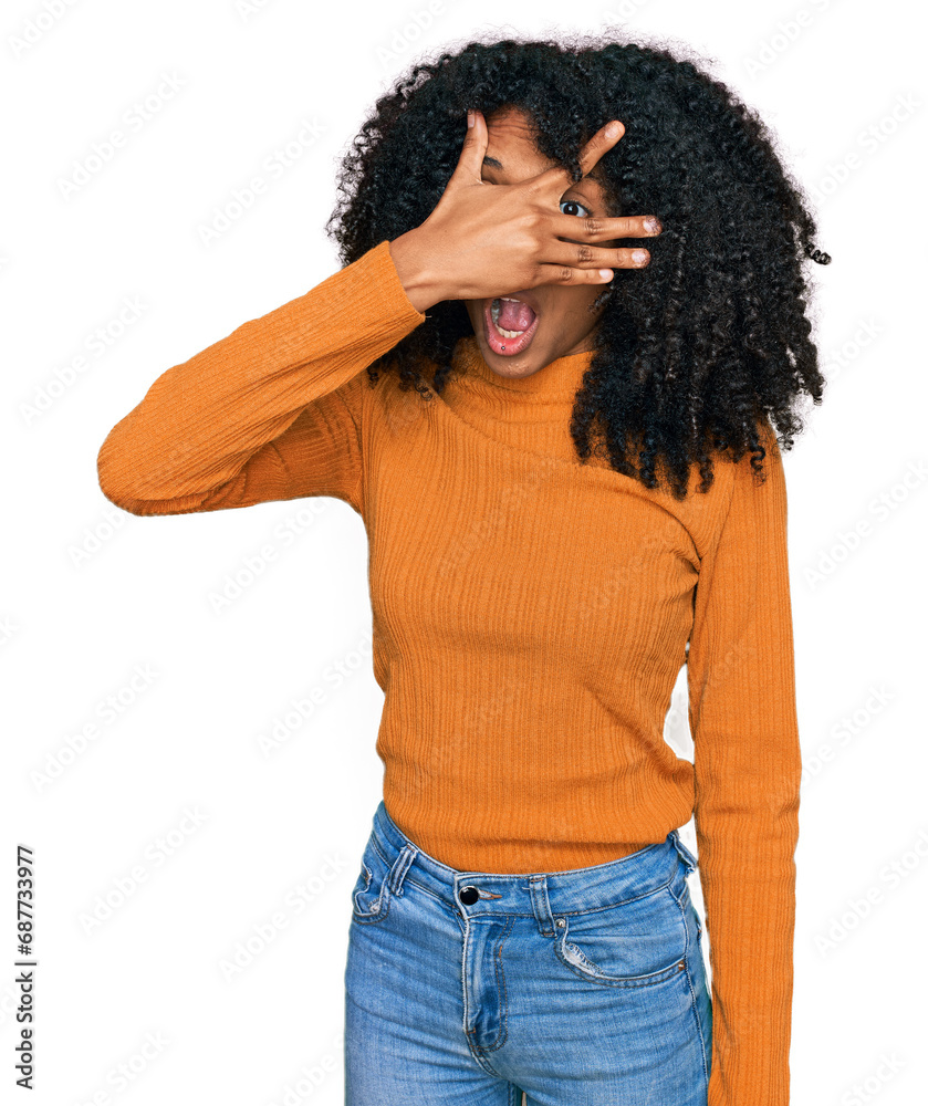 Young african american girl wearing casual clothes peeking in shock covering face and eyes with hand, looking through fingers with embarrassed expression. Young african american girl wearing casual clothes peeking in shock covering face and eyes with hand, looking through fingers with embarrassed expression.