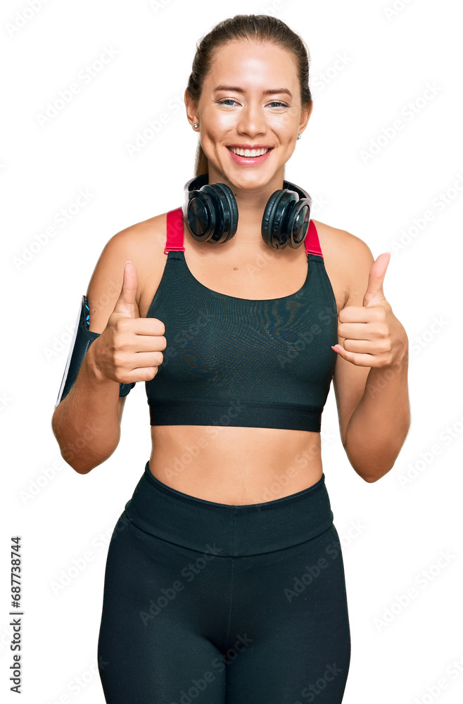 Beautiful blonde woman wearing gym clothes and using headphones success sign doing positive gesture with hand, thumbs up smiling and happy. cheerful expression and winner gesture. Beautiful blonde woman wearing gym clothes and using headphones success sign doing positive gesture with hand, thumbs up smiling and happy. cheerful expression and winner gesture.