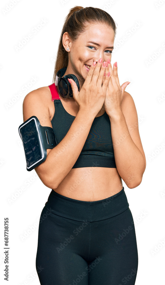 Beautiful blonde woman wearing gym clothes and using headphones laughing and embarrassed giggle covering mouth with hands, gossip and scandal concept Beautiful blonde woman wearing gym clothes and using headphones laughing and embarrassed giggle covering mouth with hands, gossip and scandal concept