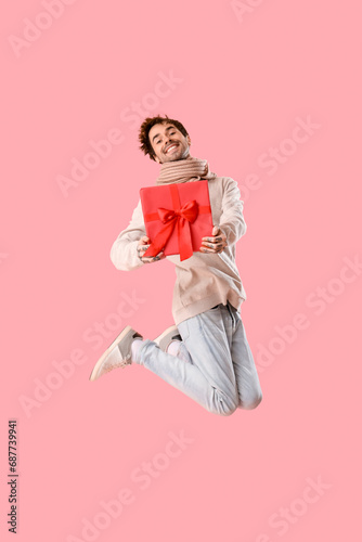 Tattooed young man with Christmas present jumping on pink background