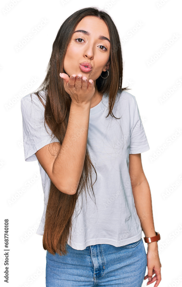 Young hispanic girl wearing casual white t shirt looking at the camera blowing a kiss with hand on air being lovely and sexy. love expression. Young hispanic girl wearing casual white t shirt looking at the camera blowing a kiss with hand on air being lovely and sexy. love expression.
