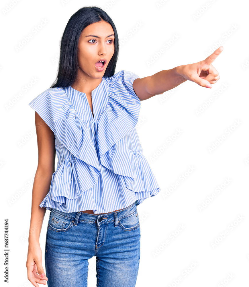 Young beautiful latin girl wearing casual clothes pointing with finger surprised ahead, open mouth amazed expression, something on the front Young beautiful latin girl wearing casual clothes pointing with finger surprised ahead, open mouth amazed expression, something on the front