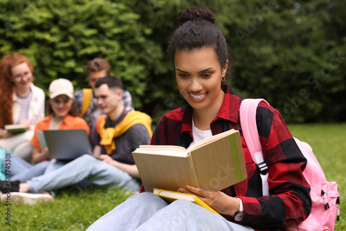Students learning together in park. Happy woman studying with notebook on green grass, selective focus