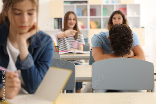 Teen problems. Lonely boy sitting separately from other students in classroom