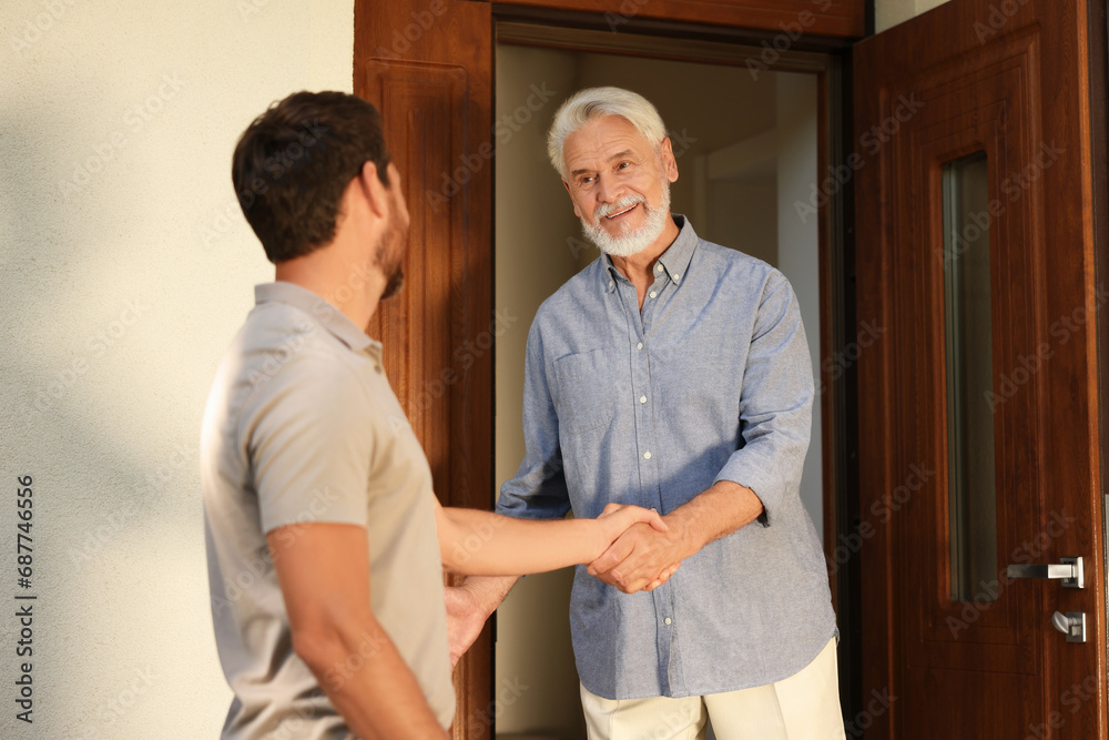 Friendly relationship with neighbours. Happy men shaking hands near house outdoors