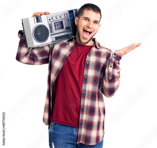 Young handsome man listening to music holding boombox celebrating victory with happy smile and winner expression with raised hands