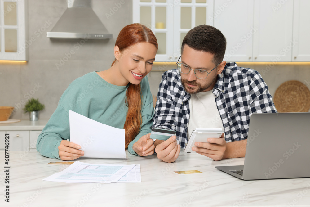 Couple with credit card calculating taxes for online payment at table in kitchen Couple with credit card calculating taxes for online payment at table in kitchen