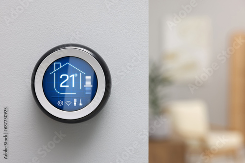 Thermostat displaying temperature in Celsius scale and different icons. Smart home device on white wall, space for text photo