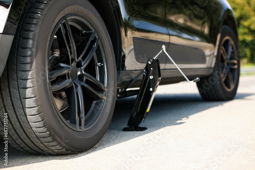 Car lifted by scissor jack on roadside outdoors. Tire puncture