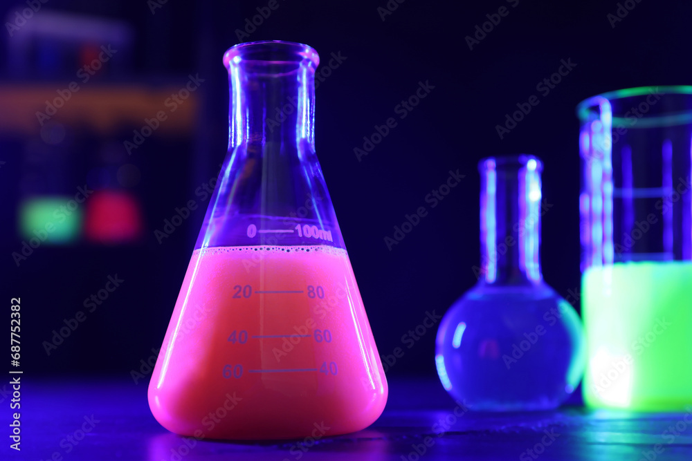 Laboratory glassware with luminous liquids on table against dark background Laboratory glassware with luminous liquids on table against dark background
