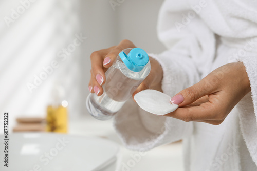 Woman pouring makeup remover from bottle onto cotton pad indoors, closeup © New Africa
