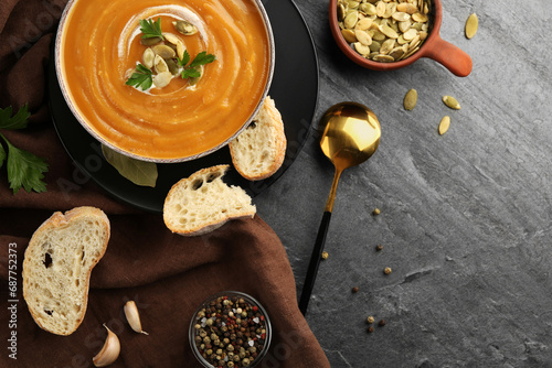 Flat lay composition with bowl of delicious pumpkin soup on grey textured table. Space for text photo