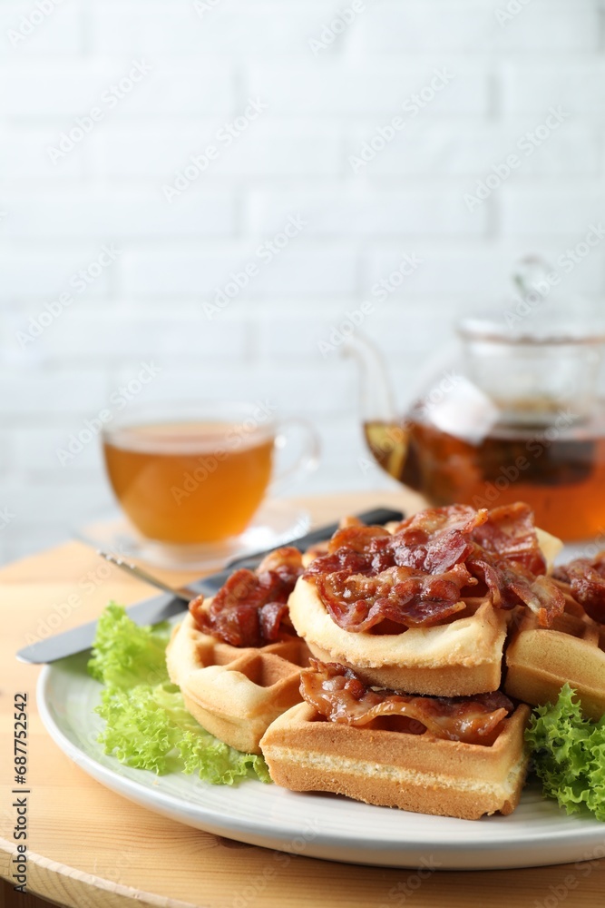 Tasty Belgian waffles served with bacon, lettuce and tea on wooden table, closeup