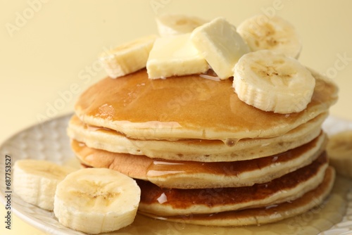 Delicious pancakes with bananas, honey and butter on beige background, closeup