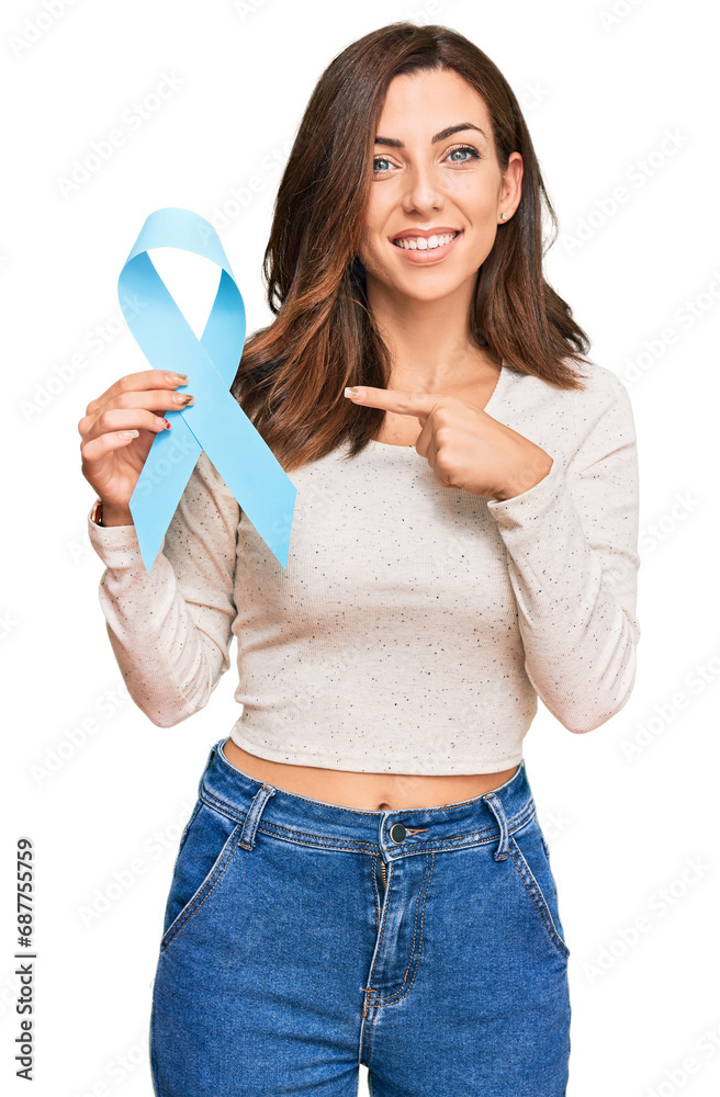 Young brunette woman holding blue ribbon smiling happy pointing with hand and finger Young brunette woman holding blue ribbon smiling happy pointing with hand and finger