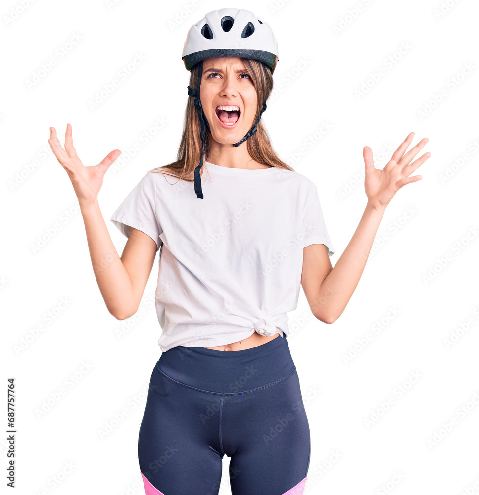 Young beautiful girl wearing bike helmet crazy and mad shouting and yelling with aggressive expression and arms raised. frustration concept. Young beautiful girl wearing bike helmet crazy and mad shouting and yelling with aggressive expression and arms raised. frustration concept.
