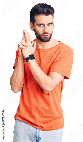 Young handsome man with beard wearing casual t-shirt holding symbolic gun with hand gesture, playing killing shooting weapons, angry face