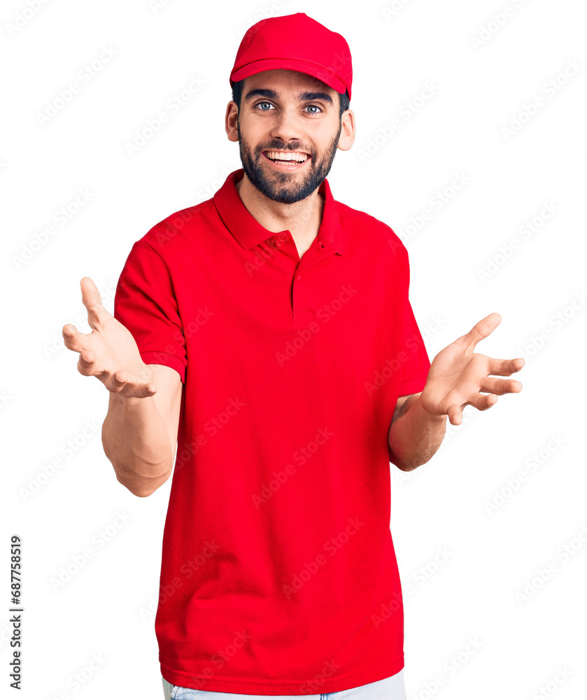 Young handsome man with beard wearing delivery uniform smiling cheerful with open arms as friendly welcome, positive and confident greetings