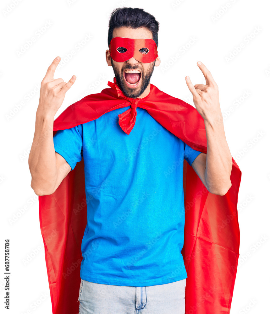 Young handsome man with beard wearing super hero costume shouting with crazy expression doing rock symbol with hands up. music star. heavy concept. Young handsome man with beard wearing super hero costume shouting with crazy expression doing rock symbol with hands up. music star. heavy concept.