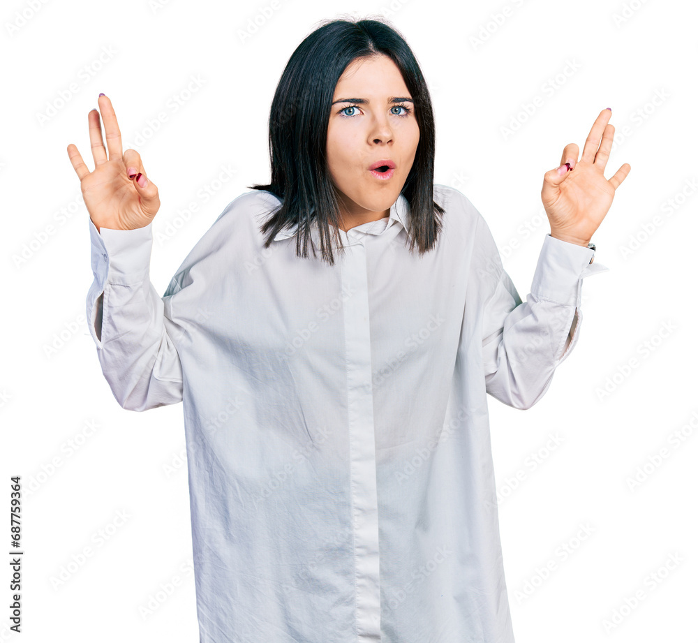 Young brunette woman with blue eyes wearing oversize white shirt looking surprised and shocked doing ok approval symbol with fingers. crazy expression Young brunette woman with blue eyes wearing oversize white shirt looking surprised and shocked doing ok approval symbol with fingers. crazy expression