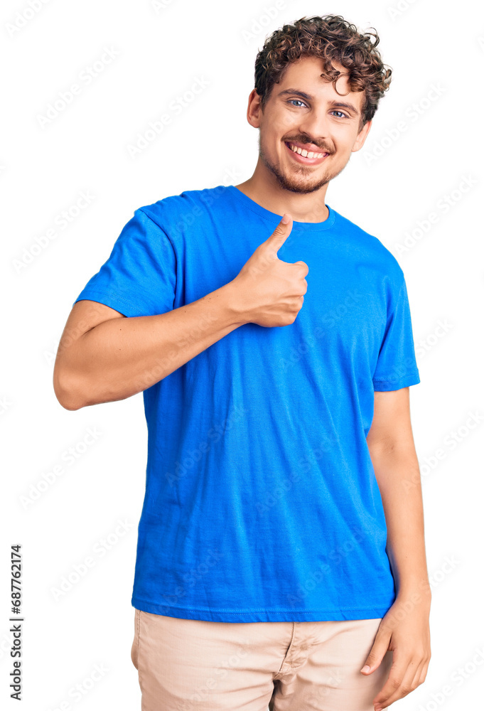 Young handsome man with curly hair wearing casual clothes doing happy thumbs up gesture with hand. approving expression looking at the camera showing success. Young handsome man with curly hair wearing casual clothes doing happy thumbs up gesture with hand. approving expression looking at the camera showing success.