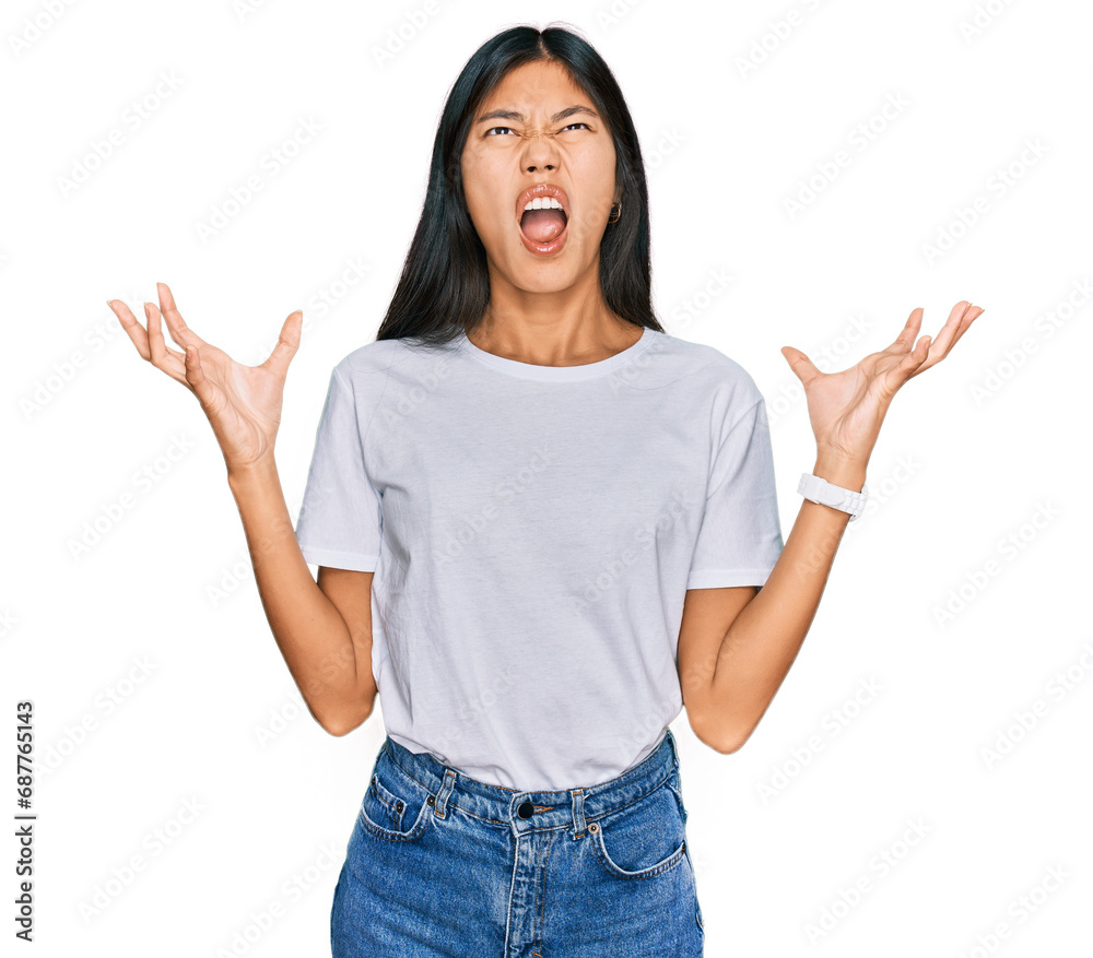 Beautiful young asian woman wearing casual white t shirt crazy and mad shouting and yelling with aggressive expression and arms raised. frustration concept. Beautiful young asian woman wearing casual white t shirt crazy and mad shouting and yelling with aggressive expression and arms raised. frustration concept.