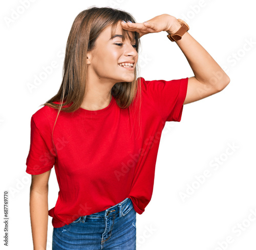 Teenager caucasian girl wearing casual red t shirt very happy and smiling looking far away with hand over head. searching concept.