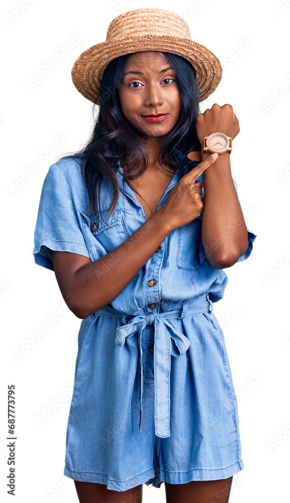 Young indian girl wearing summer hat in hurry pointing to watch time, impatience, looking at the camera with relaxed expression Young indian girl wearing summer hat in hurry pointing to watch time, impatience, looking at the camera with relaxed expression