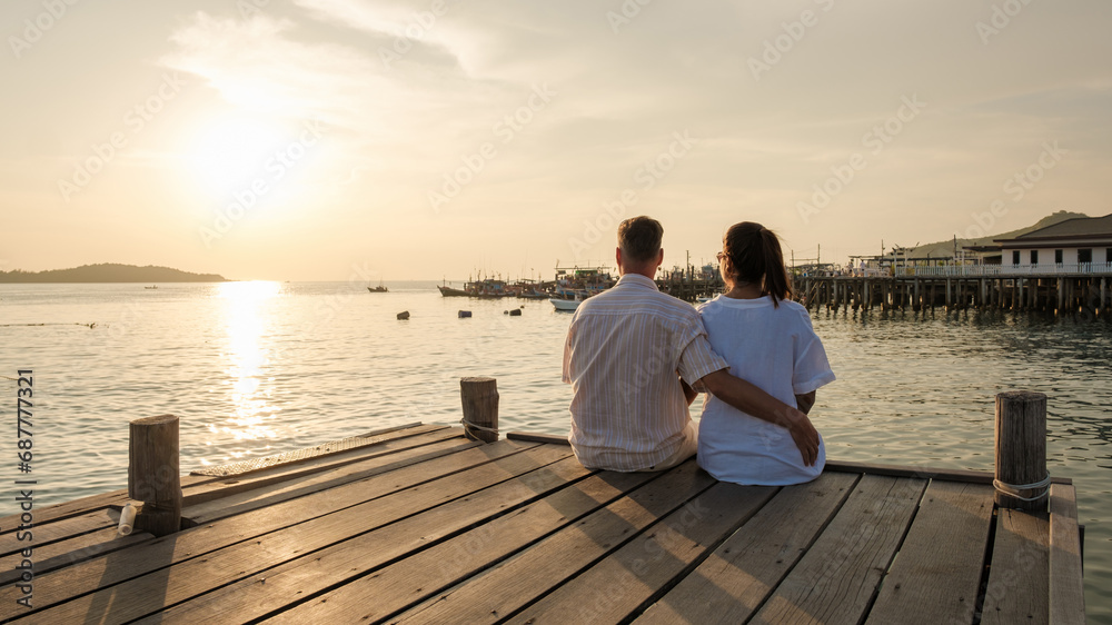 couple sitting on a wooden deck pier in the ocean during sunset in Samaesan Thailand