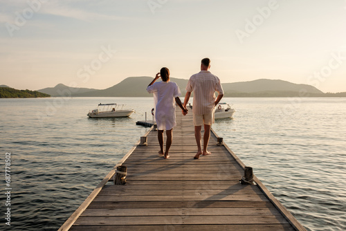 a couple walking at a wooden pier in the ocean during sunset in Samaesan Thailand photo