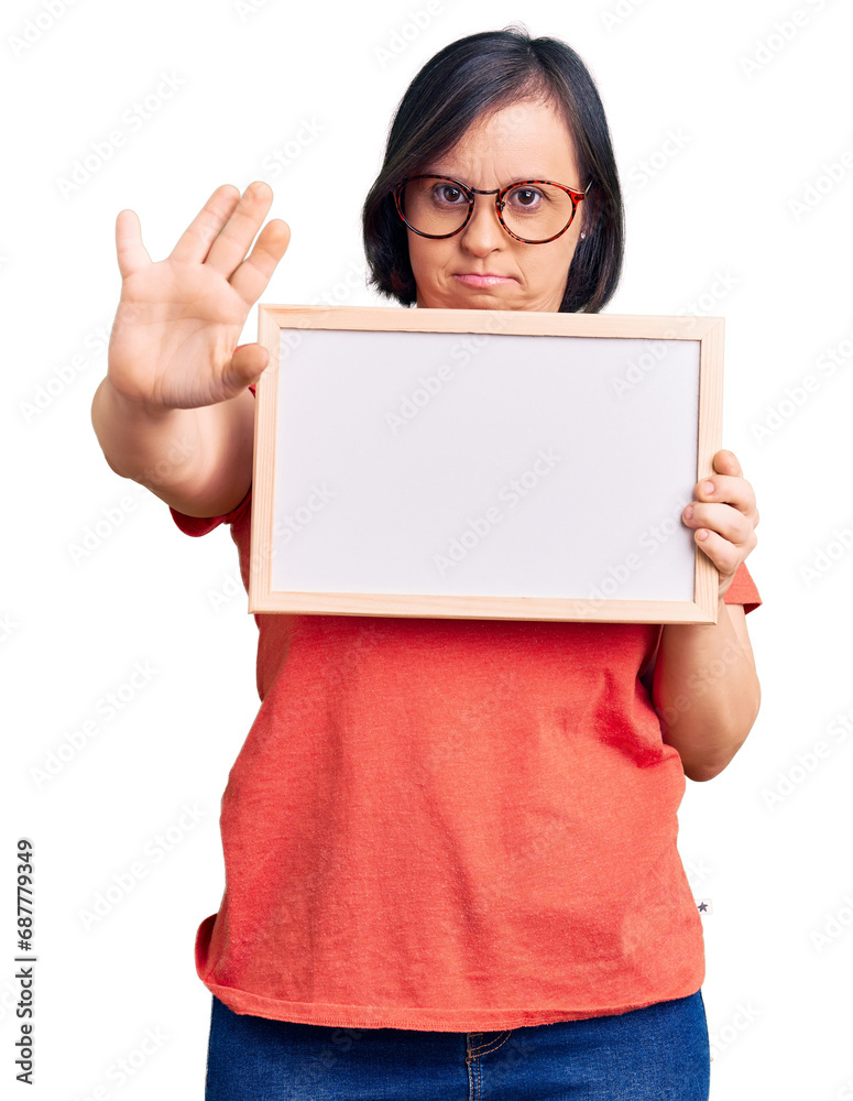 Brunette woman with down syndrome holding empty white chalkboard with open hand doing stop sign with serious and confident expression, defense gesture Brunette woman with down syndrome holding empty white chalkboard with open hand doing stop sign with serious and confident expression, defense gesture